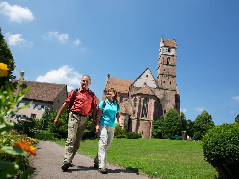 Zwei Wandernde gehen durch den Park am Kloster Alpirsbach
